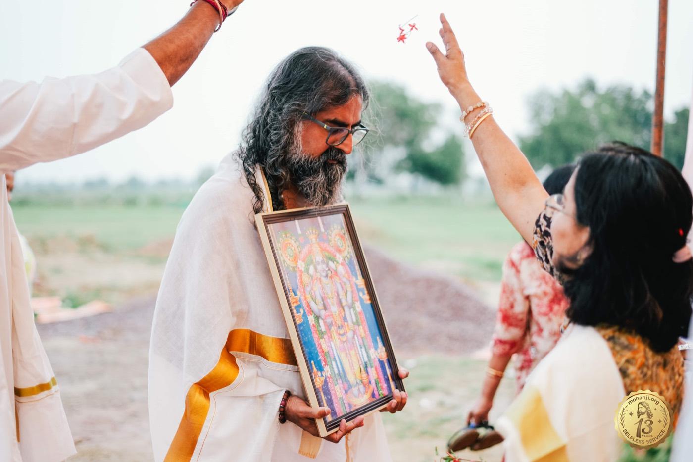 Mohanji holding a framed Guruvayurappan idol as a devotee performs aarti